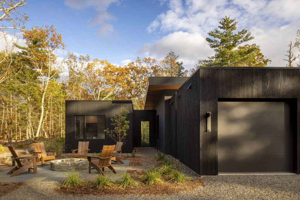 Fermata, clad in black charred siding, includes a firepit patio and an overhanging flat roof.